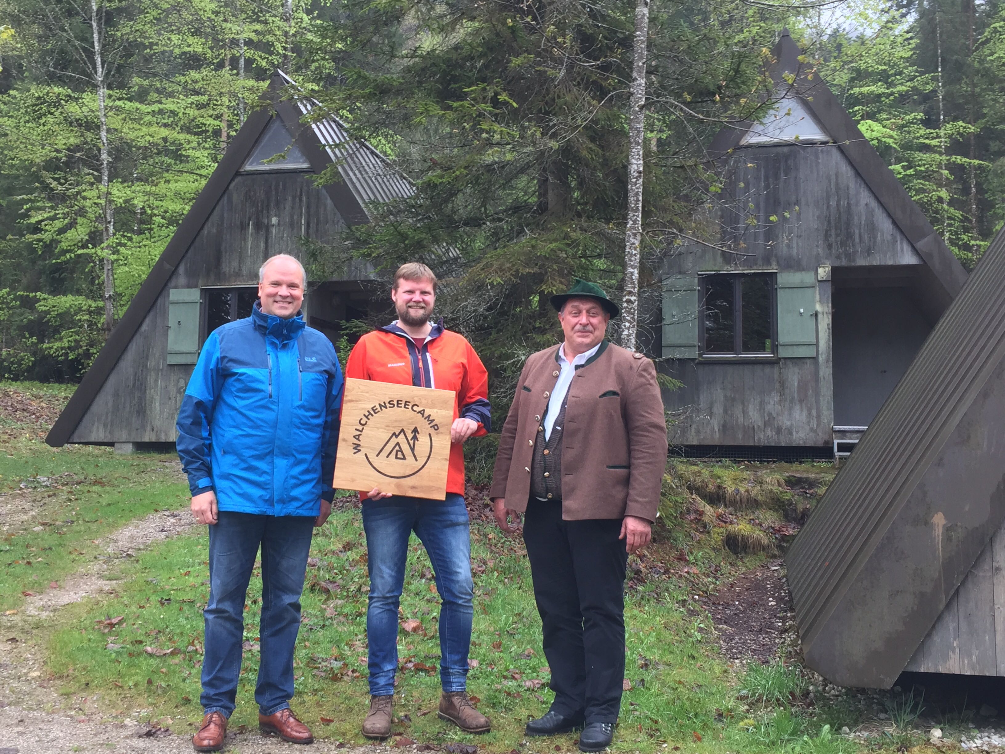 Landrat Christoph Göbel, KJR-Vorsitzender Jan Museler und Jachenaus Erster Bürgermeister Klaus Rauchenberger mit dem neuen Walchenseecamp-Logo vor den Zelthütten