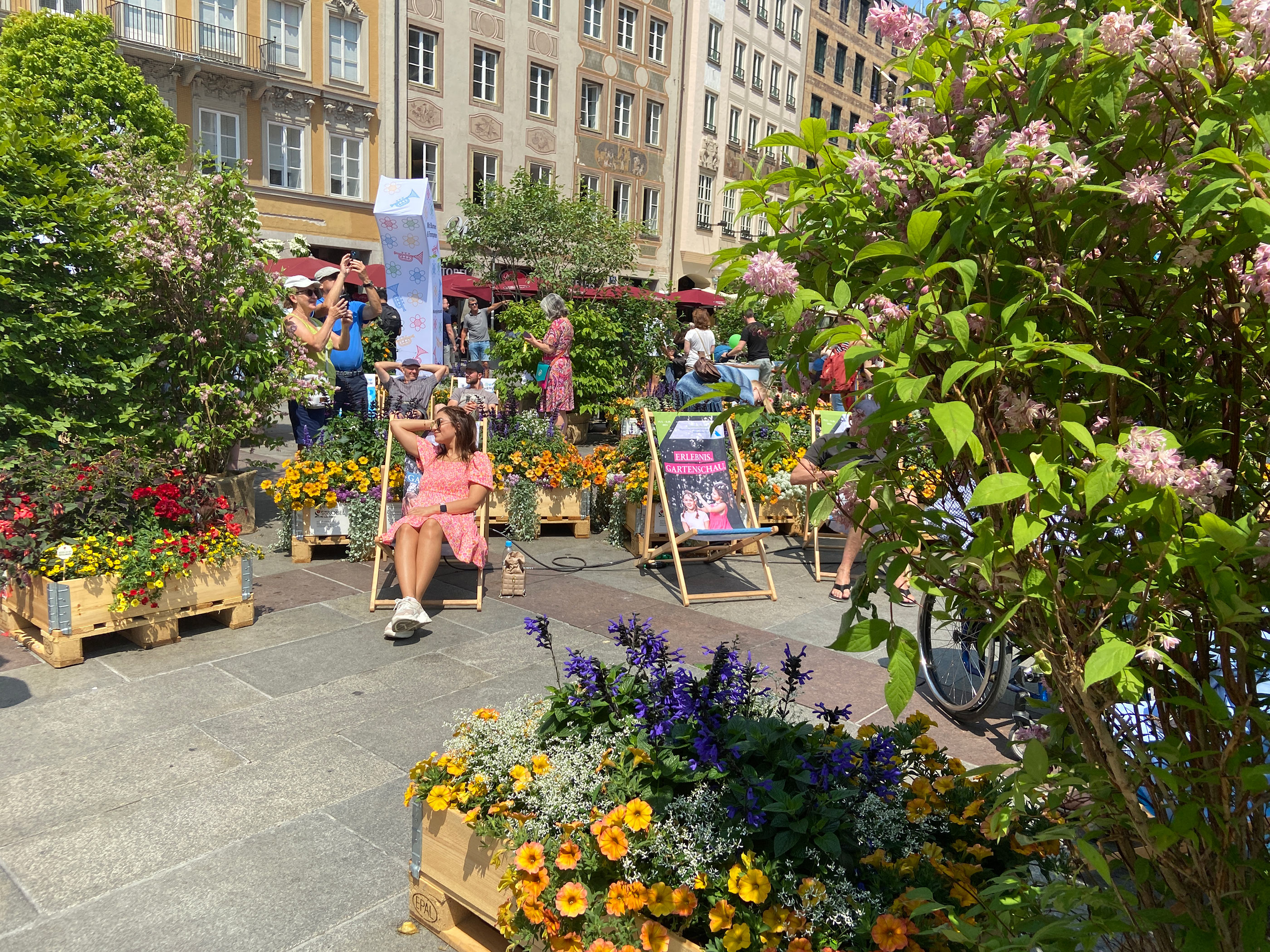 Eine Frau mit Rosa Kleid sitzt auf einem Liegestuhl im Pop-Up-Garten in der Münchner Fußgängerzone